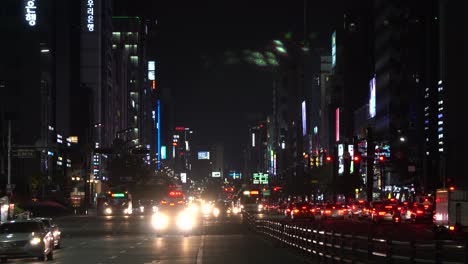 NIght-Seoul,-Ambulance-with-turned-on-siren-lights-moving-towards-the-camera-after-passing-crossroads-at-Gangnam-station,-Seoul,-South-Korea-cars-waiting-on-red-signaling-light-Seoul-night-cityscape