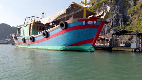 Fishing-boat-with-tire-bumpers-on-the-shores-of-an-island-linked-to-a-larger-fish-farm,-Approach-reveal-shot