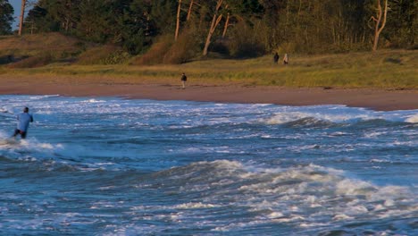 A-group-of-people-engaged-in-kitesurfing-in-sunny-autumn-day,-high-waves,-Baltic-Sea-Karosta-beach-in-Liepaja,-medium-shot