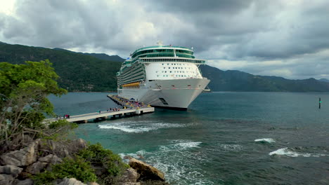 Cinematic-drone-shot-passing-rocks-and-revealing-a-docked-cruise-ship-in-the-Hatai