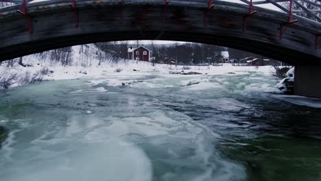 Soft-aerial-flight-beneath-brdige-above-icy-waters-in-winter-scape