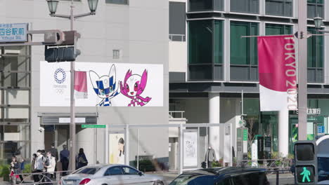 People-In-Protective-Mask-Walking-At-Sidewalk-On-A-Sunny-Day-During-Pandemic-In-Tokyo,-Japan-With-Tokyo-2020-Olympic-Banner