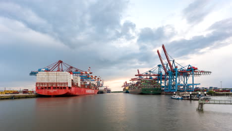 Stunning-day-to-night-time-lapse-of-Port-of-Hamburg-while-huge-container-ships-get-loaded-and-unloaded-by-cranes-while-sun-sets-in-Hamburg,-Germany