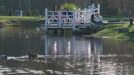 Familien-Füttern-Enten-Im-Birute-Park-In-Palanga-An-Einem-Sonnigen-Frühlingstag,-Während-Sie-Auf-Einem-Holzsteg-Stehen