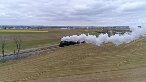 A-Drone-View-of-a-Steam-Locomotive-With-Passenger-Coaches-Approaching-With-a-Full-Head-of-Steam-over-Countryside-on-a-Winter-Day