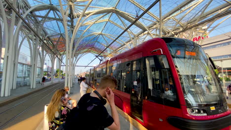 Toma-En-Cámara-Lenta-Del-Tranvía-Que-Llega-A-La-Estación-De-Tranvía-En-Lodz-Durante-El-Día-Soleado---Personas-Que-Ingresan-Y-Usan-Máscara-Facial-Durante-La-Pandemia-De-Covid-19-En-Polonia