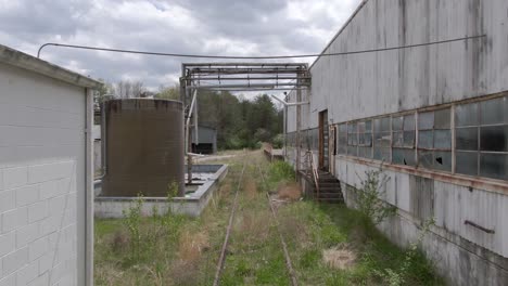 Imágenes-De-Drones-Avanzando-Sobre-Vías-De-Tren-Cubiertas-De-Maleza-En-Una-Fábrica-Abandonada