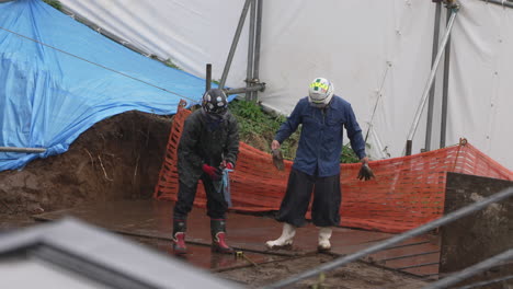 Dos-Trabajadores-De-La-Construcción-Con-Cascos-Y-Botas-De-Goma-Trabajando-Bajo-La-Lluvia-Torrencial