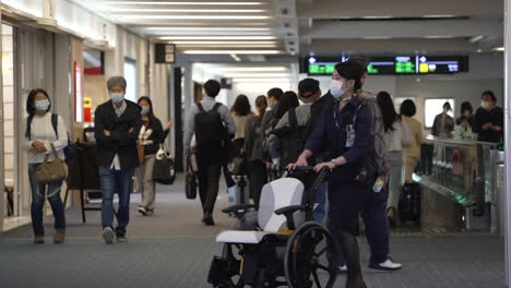 Azafata-De-Vuelo-Enmascarada-Empujando-Una-Silla-De-Ruedas-Vacía-En-El-Aeropuerto-De-Tokio,-Japón