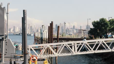 The-deckhand-of-a-moored-ship-walking-across-a-pier-to-the-dockyard,-in-the-distance-the-Panama-Canal-and-the-beautiful-buildings-of-the-modern-cityscape-of-Panama-City