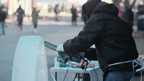 Side-view-of-artist-shaping-ice-arch-with-chainsaw-at-winter-festival