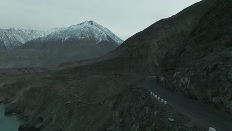 Aerial-Circle-Dolly-View-Of-Mountainside-Road-In-Hunza-Valley-With-Coaches-Travelling-Along-And-Snow-Capped-Mountains-In-Background