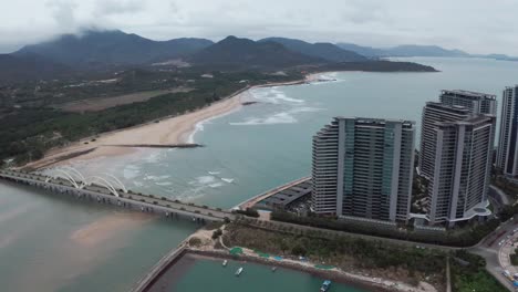 Fliegen-Sie-über-Den-Hotelresortkomplex-Auf-Einer-Künstlichen-Insel-Mit-Langem-Strand-Und-Bergrücken-Im-Hintergrund