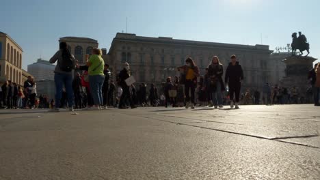 Ground-surface-pov-of-people-walking-at-Duomo-square-in-Milan-with-Vittorio-Emanuele-II-equestrian-monument-in-background,-Italy