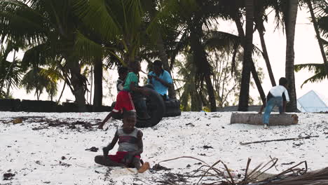 Un-Niño-Africano-Tratando-De-Hacer-El-Pino-En-La-Playa,-Otros-Niños-Juegan-Detrás