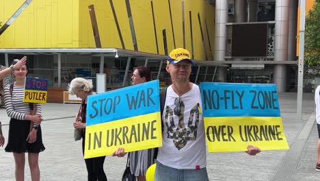 Ein-Herr-Hält-Sich-An-Einem-Schild-Fest,-Auf-Dem-Steht:-„Krieg-In-Der-Ukraine-Stoppen“-Und-„Flugverbotszone“-über-Dem-Luftraum-In-Der-Ukraine-Bei-Der-Friedlichen-Kundgebung-Am-Downtown-Brisbane-Square,-Queensland,-Australien