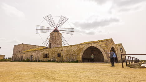 Turista-Visitando-El-Edificio-Antiguo-Con-La-Torre-Del-Molino-De-Viento-Durante-El-Día-Nublado-En-La-Isla-De-Sicilia-En-Italia,-Europa---Disparo-De-Lapso-De-Tiempo