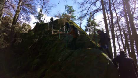 Group-of-hikers-with-backpacks-climb-a-rocky-path-to-the-top-of-a-mountain-on-a-cold-spring-day-with-falling-snow-and-sun-in-a-wooded-landscape