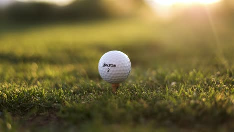 Pelota-De-Golf-Srixon-Colocada-En-El-Tee-Box-En-El-Campo-De-Golf,-Puesta-De-Sol-Con-Bengala-Solar