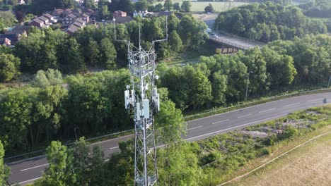 Antena-De-Torre-De-Radiodifusión-5g-En-El-Campo-Británico-Con-Vehículos-Que-Viajan-Por-Carreteras-Vista-Aérea-Inclinada-Hacia-Abajo