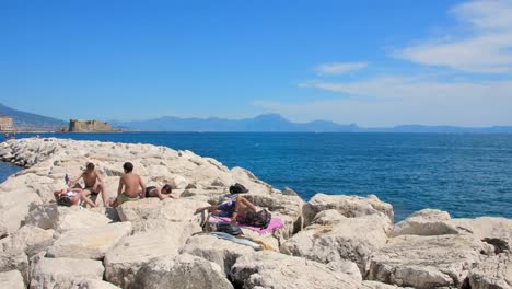 La-Gente-Toma-El-Sol-En-La-Rocosa-Costa-Mediterránea-En-Nápoles,-Italia