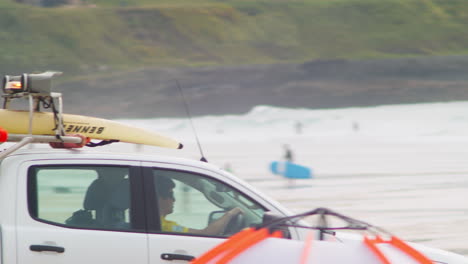 RNLI-Coast-Guard-Driver-Driving-Pickup-Truck-With-Surfboard-at-Fistral-Beach,-Cornwall---close-up