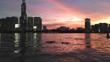 Preciosa-Puesta-De-Sol-Dorada-En-La-Ciudad-De-Ho-Chi-Minh,-Vuelo-Bajo-De-Drones-Sobre-El-Río-Saigón