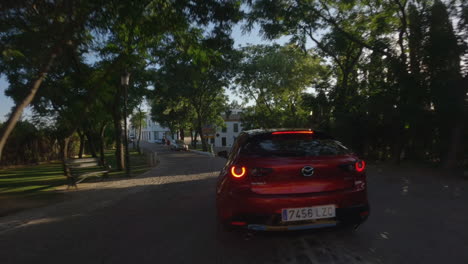 Dinámica:-El-Dron-Fpv-Se-Alinea-Detrás-Del-Automóvil-Mazda-Rojo-Conduciendo-Por-El-Parque