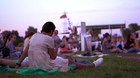 Mädchen-Auf-Einem-Festival-Im-Freien-Auf-Ihrem-Handy-Mit-Litauischer-Flagge-Hinter-Sich