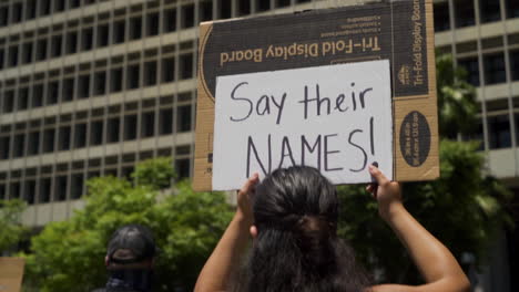 A-Woman-holds-up-a-sign-that-says-"Say-Their-Names,"-at-a-BLM-protest-outside-City-Hall