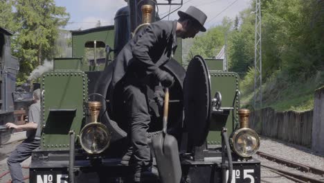 Young-man-shoveling-and-emptying-ashes-from-steam-locomotive-Blonay-Chamby-museum-track,-Switzerland