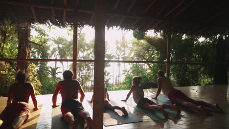 Una-Familia-De-Viajeros-Disfrutando-De-Una-Meditación-Al-Atardecer-Y-Una-Sesión-De-Yoga-En-Un-Porche-De-Madera-Con-Vista-A-La-Selva-Tropical-Y-La-Jungla-Que-Conduce-A-La-Playa