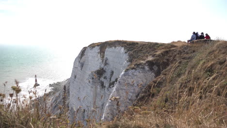 UK-July-2018---a-group-of-tourists-sit-on-the-edge-of-Beachy-Head-cliff-top,-looking-out-at-the-sea-and-pointing