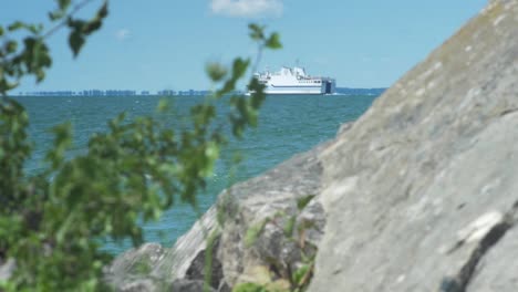 Rack-Fokussierung-Von-Einem-Großen-Stein-Am-Strand-Auf-Eine-Weiße-Fähre,-Die-Im-Hintergrund-Im-Meer-Fährt