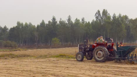 A-farmer-operates-his-tractor-in-the-field-near-a-Eucalyptus-forest