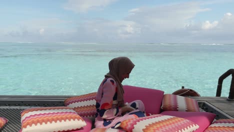 Woman-sits-in-an-outdoor-lounge-area-on-the-ocean-and-tosses-flowers-into-the-air