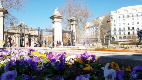 People-entering-the-gate-to-Retiro-Park,-Madrid,-with-Puerta-de-Alcála-in-the-background,-slow-motion