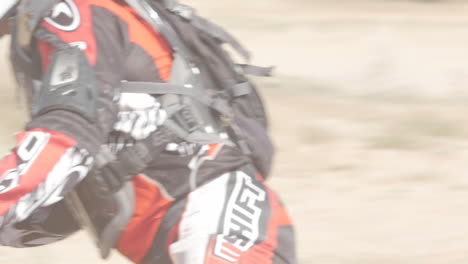 SLOW-MOTION:-A-dirt-biker-rides-his-red-motorcycle-through-the-desert-and-whips-around-a-berm