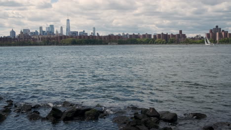 From-the-Brooklyn-side-of-the-East-River,-this-shot-pans-from-the-Brooklyn-bridge-to-midtown-showing-the-One-World-Trade-Center,-housing,-Factories,-the-Empire-State-building-and-more