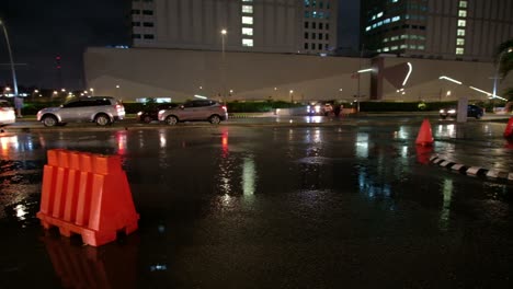 Outdoor-evening-scene-showing-vehicular-traffic-in-a-drizzle-around-a-commercial-district-within-Quezon-City-in-Metro-Manila,-Philippines