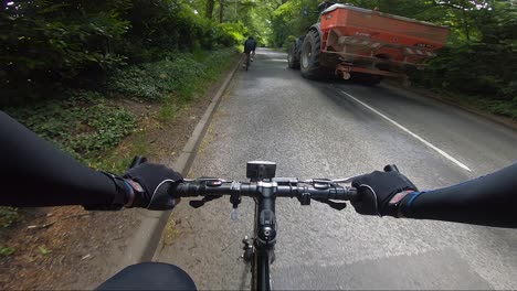 POV-Ansicht-Radfahren-Auf-Der-Straße,-Das-Von-Einem-Großen-Traktor-Und-Einem-Weißen-Auto-überholt-Wird