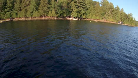 Slow-Motion---Cottage-Family-Drives-Boat-to-Dock-after-Water-Ski,-Man-Swims-to-Shore-in-Blue-Lake-at-Summer-Sunset