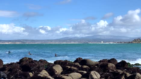 Surfers-in-wet-suits-waiting-to-catch-a-wave-while-a-father-and-son-is-exploring-ocean-tide-pools-in-Monterey-County