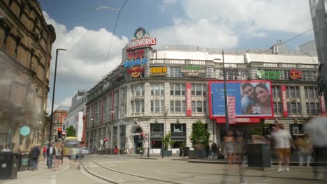 Timelapse-of-Printworks-Greater-Manchester-City-summer-sunny-day-tourist-attraction-with-people-walking-in-foreground-with-trams-and-buses-public-transport-clouds-passing-by-landmark-4K-25p