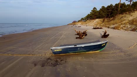 Aerial-view-of-Baltic-sea-coastline-at-Bernati-beach-in-Latvia,-coastal-pine-forest,-flying-forward-over-white-sand-beach-and-fisherman-boat,-wide-angle-establishing-drone-shot