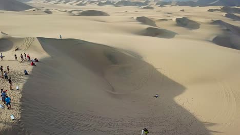 Aerial,-orbit,-drone-shot,-of-people-sandboarding,-on-sand-dunes,-near-the-Huacachina-oasis-village,-on-a-sunny-day,-in-southwest-Peru