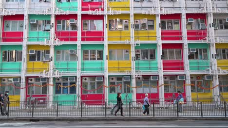 Se-Ve-A-Los-Peatones-Pasar-Frente-A-Una-Colorida-Fachada-De-Un-Edificio-De-Viviendas-Públicas-En-Hong-Kong.