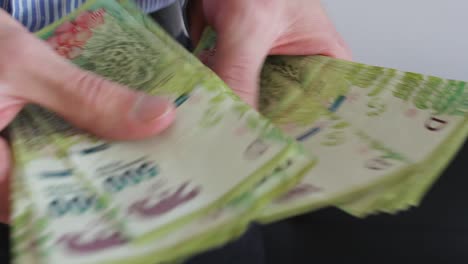 Young-businessman-counting-Argentine-cash-money-"pesos".-Close-up