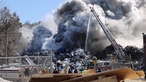 A-Thick,-Dark-Cloud-of-Smoke-Rises-from-a-Scrap-Pile-Fire-with-an-Active-Firetruck-on-Scene-on-a-Sunny-Day