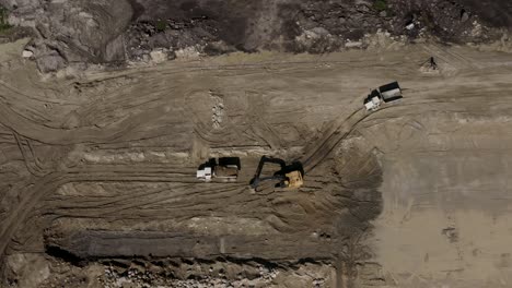 Toma-Aérea-En-Círculos-De-Una-Excavadora-John-Deere-450d-Cargando-Tierra-En-Un-Camión-De-Roca-En-Un-Sitio-De-Construcción